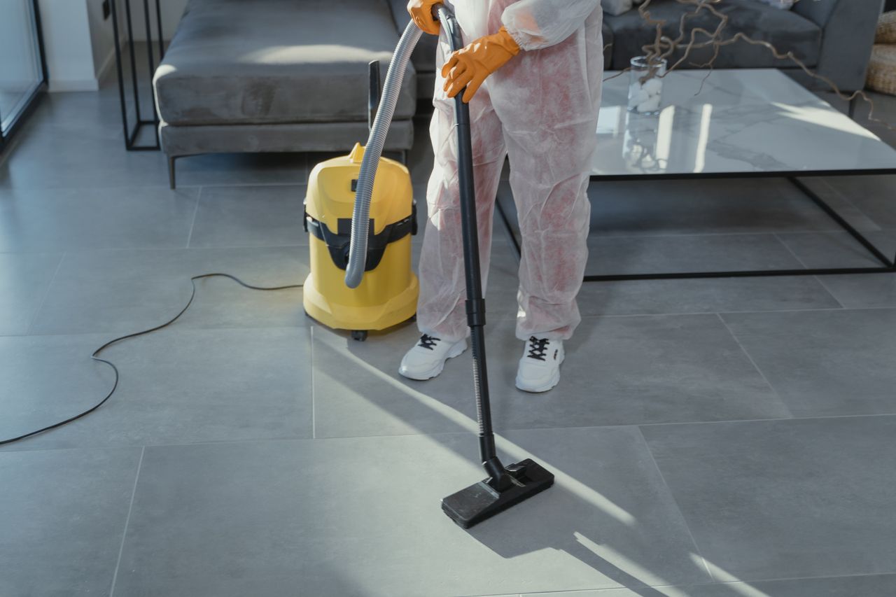 services-03 A professional cleaner in protective gear vacuuming the floor in a modern living room.